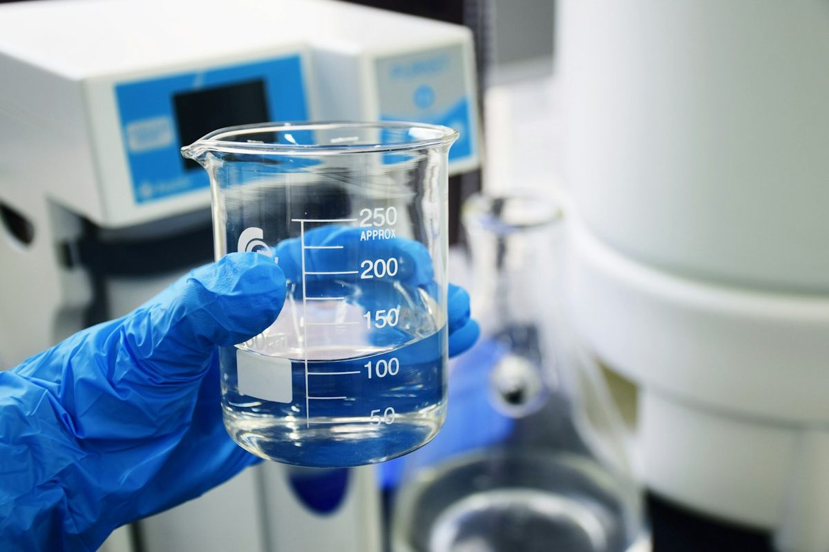 Gloved hand holding a laboratory beaker of water