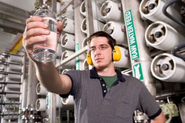 Engineer holding up a glass of treated water in a reverse osmosis plant